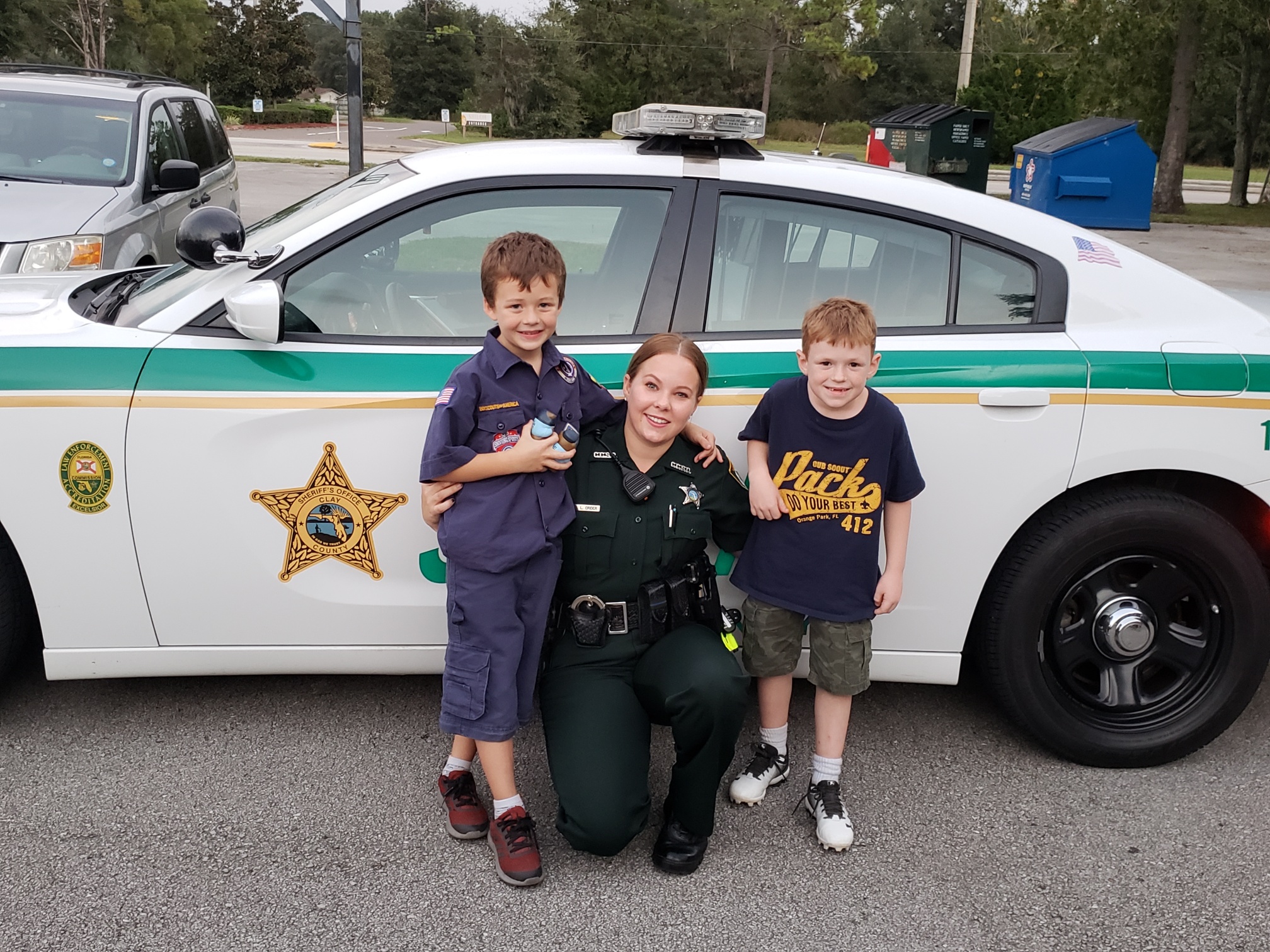 Sheriff hugging two children next to car